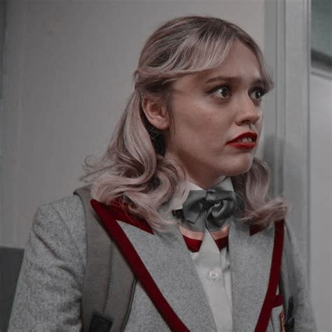 A Woman With Blonde Hair Wearing A Grey Jacket And Bow Tie Looking At The Camera