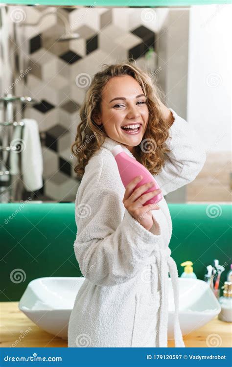 Image Of Young Woman In Housecoat Holding Body Lotion After Shower