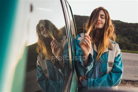 Pretty Young Woman Leaning On Car And Touching Hair In Nature