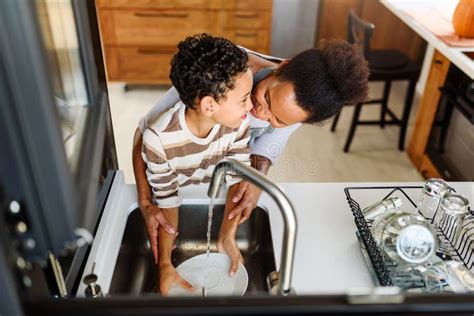 O Filho Está Ajudando A Mãe Na Cozinha Lavando Pratos Foto De Stock