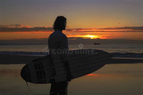 Surfer Holding Surfboard Looking At The Sunrise On The Seashore Stock