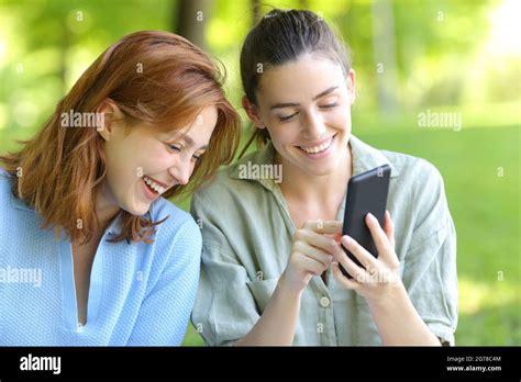 Two Happy Friends Laughing Loud Checking Smart Phone In A Park Stock Photo Alamy
