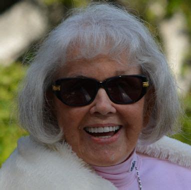 An Older Woman Wearing Sunglasses And A White Fur Stoler Smiles At The