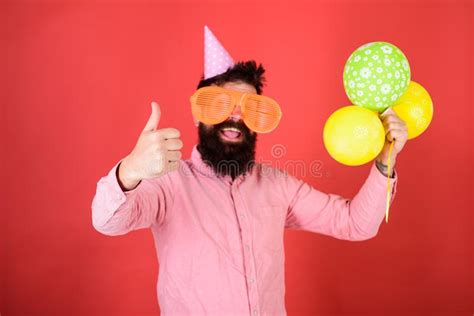 man with beard and mustache on happy face holds bunch of air balloons red background hipster