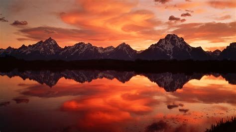 The Mountains Are Reflected In The Still Water At Sunset With Red And