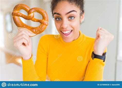 Young African American Woman Eating German Salty Pastry Pretzel Screaming Proud And Celebrating