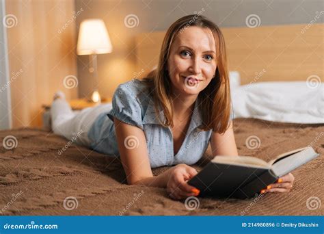 Happy Beautiful Woman Reading Book Lying On Bed In Cozy Bedroom And