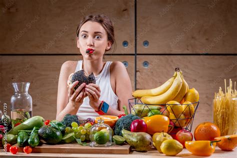 Hungry Woman Eating Black Burger At The Table Full Of Fruits And Vegetables On The Wooden