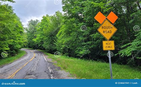 Rough Road Ahead Sign With Bumpy Pothole Patched Asphalt And Cloudy