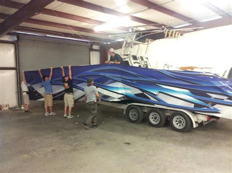 Three Men Standing Next To A Blue And White Boat In A Garage With Its