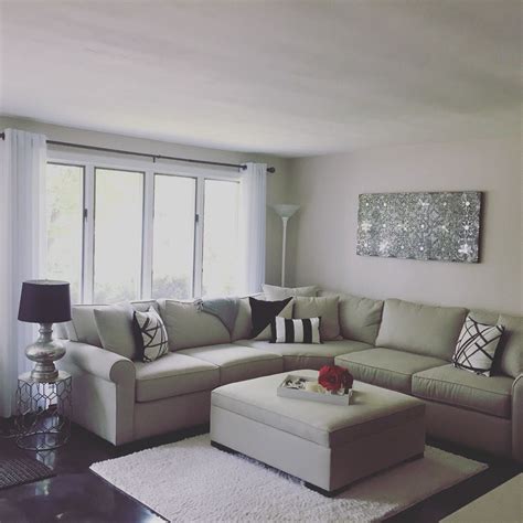 A lively living room with white furniture a pretty boho living room with a grey sofa, a white table, layered rugs, neutral tables, some candles and an artwork. Neutral Glam Living Room