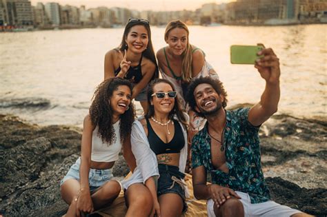 Multiracial Group Of People Enjoying Weekend Beach Activities Taking Selfies And Hanging Out