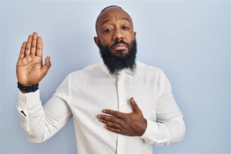 African American Man Standing Over Blue Background Swearing With Hand