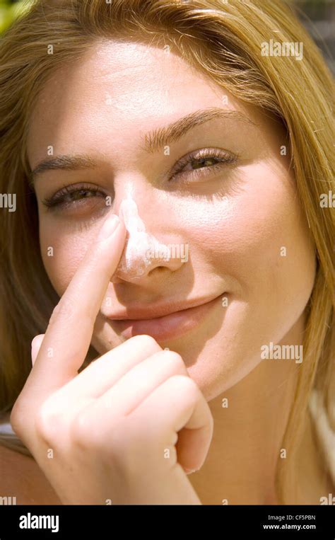 female with long straight blonde hair rubbing cream into nose looking to camera smiling stock