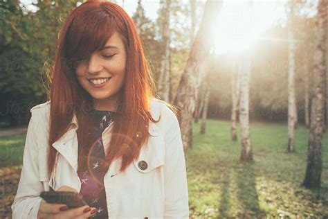 Redhead Woman Using Her Phone In The Park By Stocksy Contributor Jovo Jovanovic Stocksy