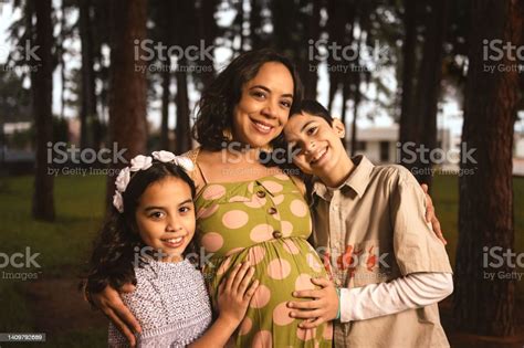 Pregnant Latin Mom Hugging Her Son And Daughter In Pine Forest Looking