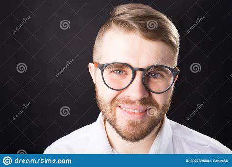 Close Up Portrait Of Smiling Handsome Bearded Man In Stylish Glasses Standing Against Black Wall