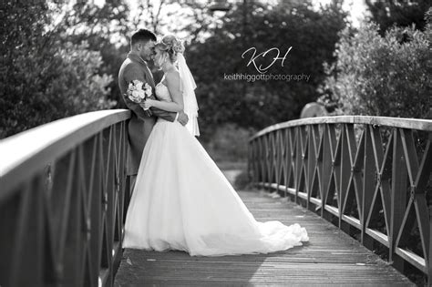 A Bride And Groom Standing On A Bridge In Black And White With Trees
