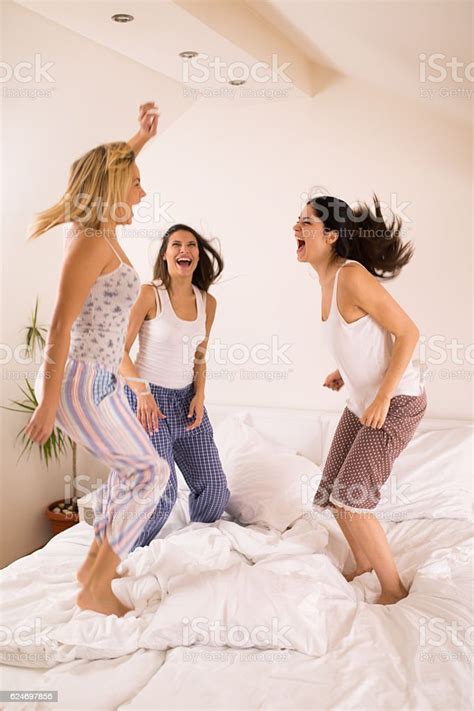 Playful Women Having Fun At Slumber Party Jumping On Bed Stock Photo