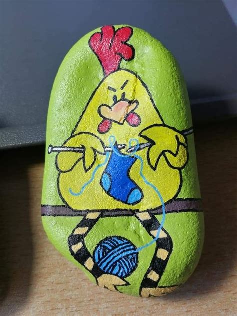 A Painted Rock With An Image Of A Chicken Holding A Yarn Ball And