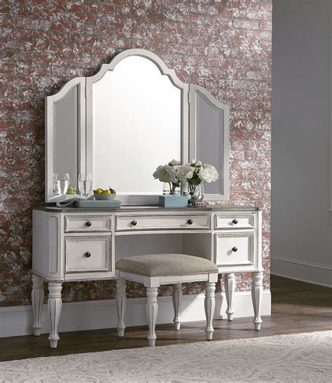 Bedroom dressing area features a nook filled with a gold floating makeup vanity with drawer under a bold leaf mirror paired with a gold velvet tufted pouf atop a white sheepskin rug. Magnolia Adjustable Arch Top 3-Panel Vanity Mirror in ...