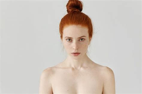A Naked Woman With Red Hair And Blue Eyes Is Posing In Front Of A White Background