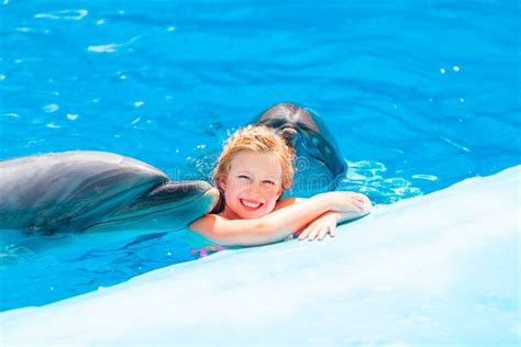 Happy Little Girl Swimming With Dolphins In Dolphinarium Stock Photo