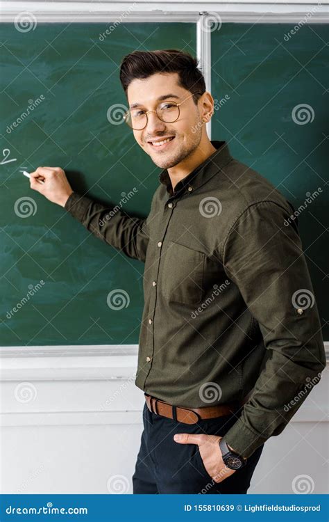 Smiling Male Teacher Looking At Camera And Writing On Chalkboard Stock