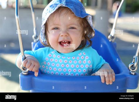 Portrait Of Laughing Baby Girl Sitting On Blue Baby Swing Stock Photo