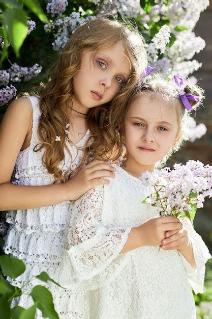 premium photo two girl poses in a lilac bush in the spring romantic portrait of a girls in