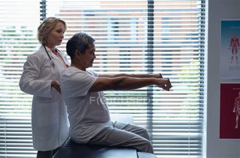 Side View Of Mature Caucasian Female Doctor Examining Senior Mixed Race