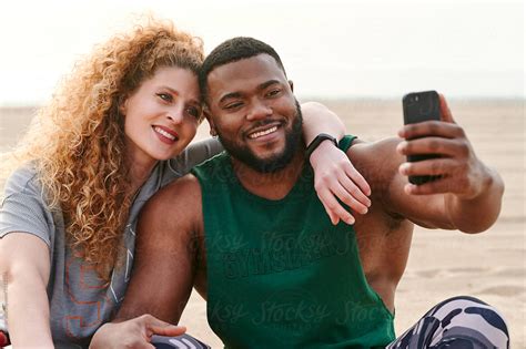 Fit Young Couple Smiling And Taking A Selfie Together While Sitting At The Beach After Workout