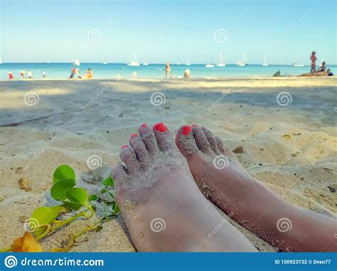 Womans Feet On The Sandy Beach With Coral Red Manikure View On The