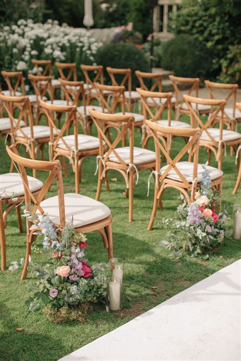 Rows Of Wooden Chairs With Flower Arrangements On The Grass At An Outdoor Wedding Ceremony Venue