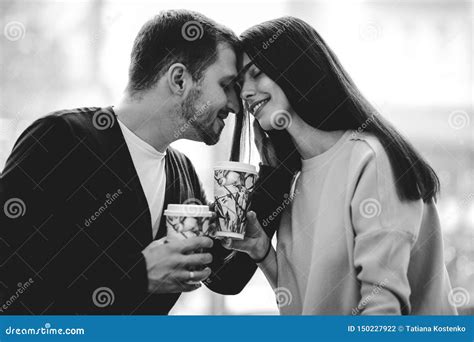 loving couple is siting face to face on the background of window and holding cups in their hands