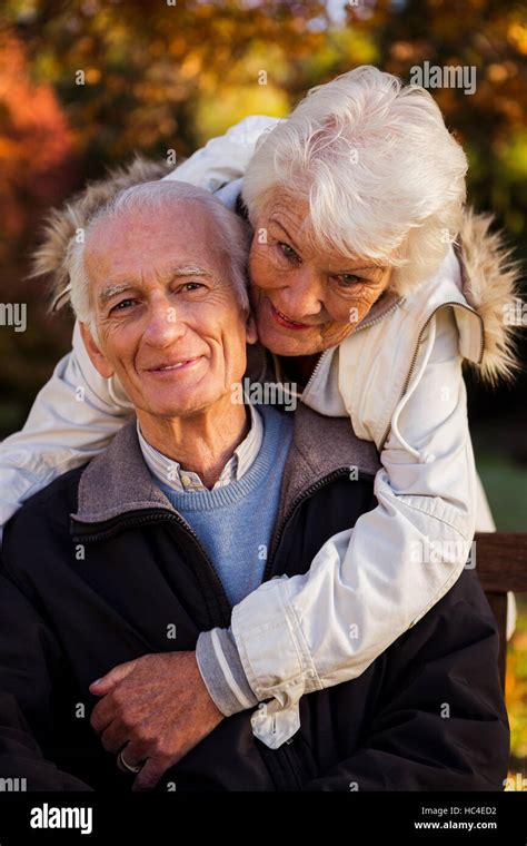 An Elderly Woman Hugs Her Husband Sitting On The Bench Looking At