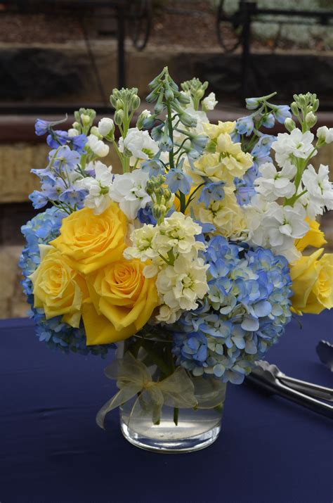 A Vase Filled With Yellow And Blue Flowers On Top Of A Table Next To