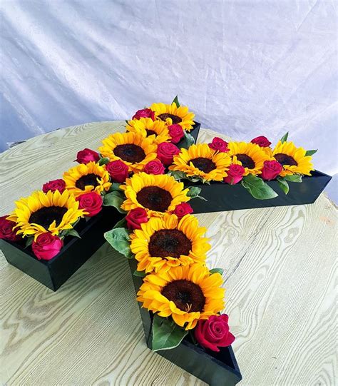 A Cross Made Out Of Sunflowers On Top Of A Table With Red Roses