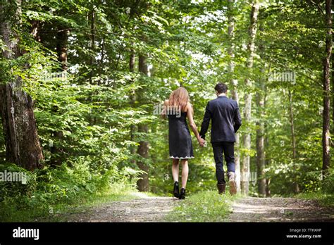 Rear View Of Couple Holding Hands While Walking On Dirt Road In Forest