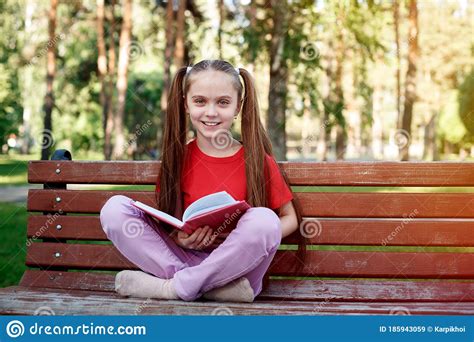 Portrait Of Cute Smiling Little Girl Sitting On The Wooden Bench In