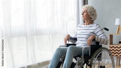 pensive sick disabled old lady sit in wheelchair look in distance feel lonely at home or