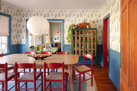 A Dining Room Table With Red Chairs In Front Of A Wallpapered Living Room