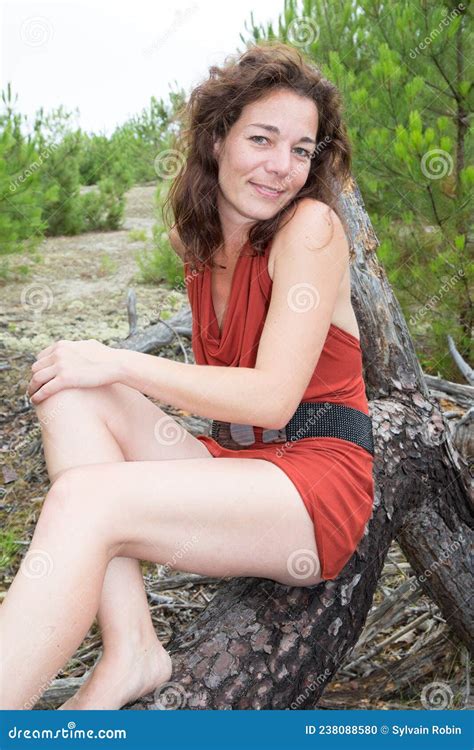 beautiful 40 year old brunette woman middle aged sit on tree branch on sea beach coast stock