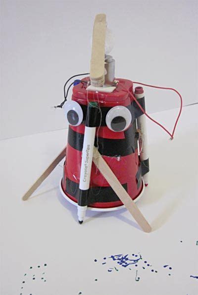 A Red And Black Robot Made Out Of An Electrical Device With Two Sticks
