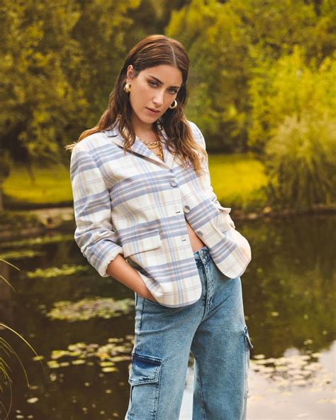 A Woman Is Standing By The Water Wearing Jeans And A Plaid Shirt With
