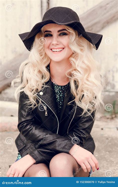 The Girl In The Black Hat And Leather Jacket Sits And Smiles Stock