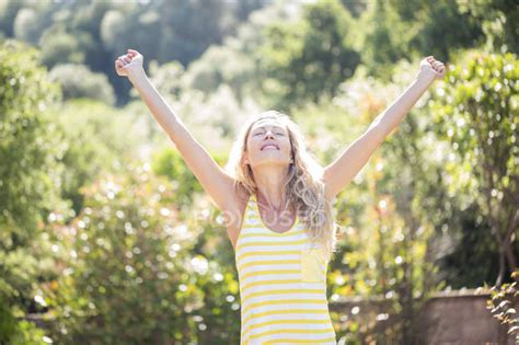 Happy Woman With Arms Outstretched And Eyes Closed Standing In Garden