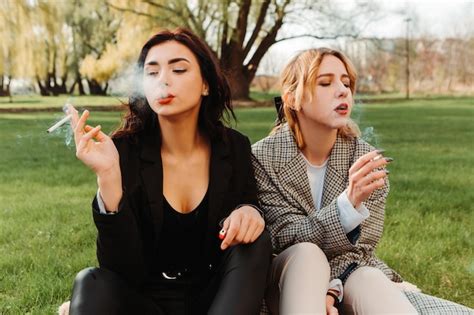Premium Photo Two Pretty Women Friends Sitting On Grass Smoking