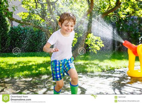 Little Kid Boy Playing With A Garden Hose Water Sprinkler