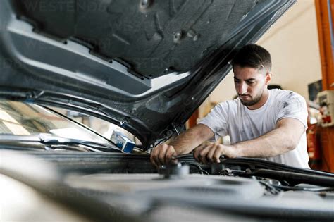 Young Man Repairing Car While Standing In Auto Repair Shop Stock Photo